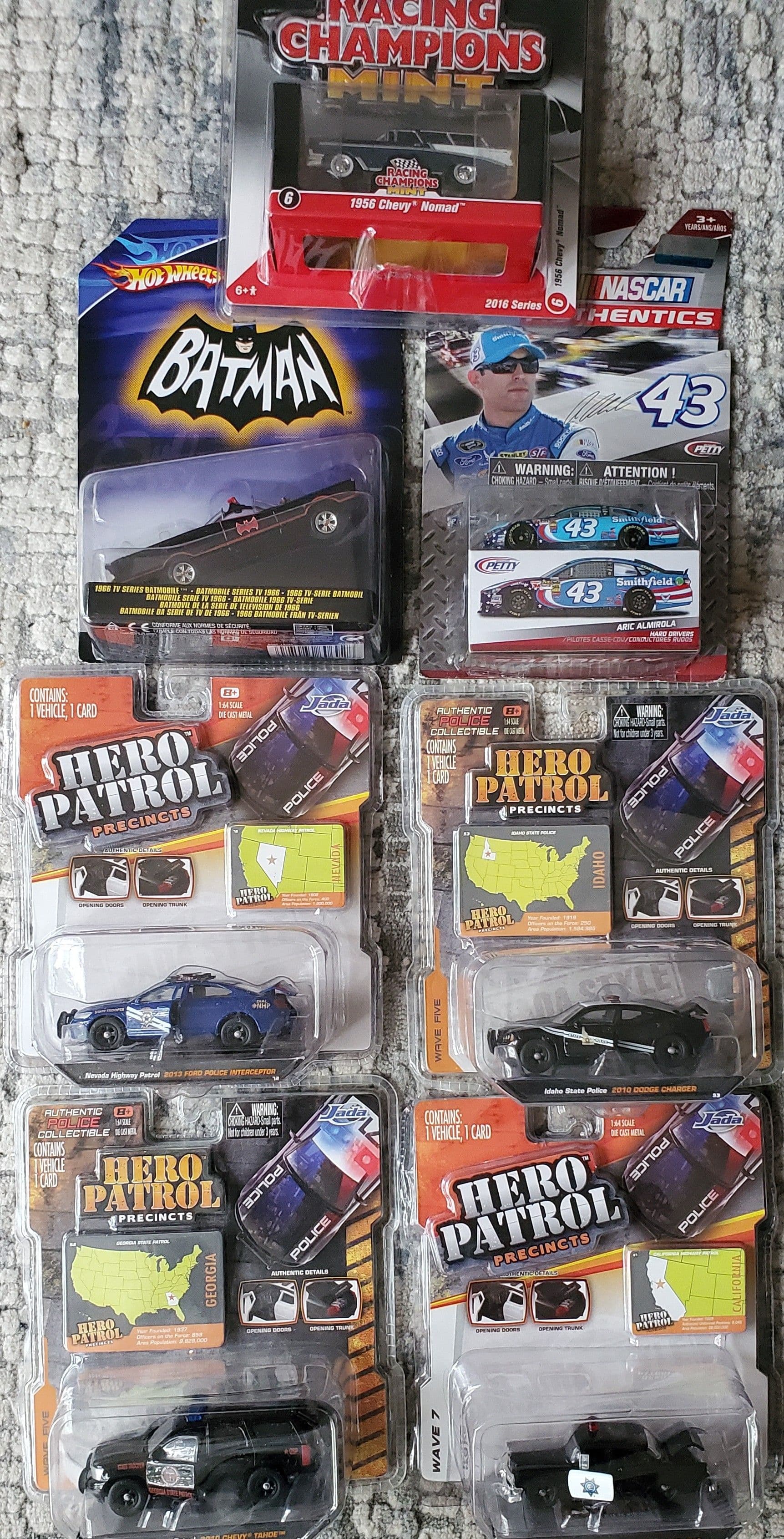 Mixed diecast car lot featuring Racing Champions Mint 1956 Chevy Nomad, Hot Wheels 1966 TV Series Batmobile, NASCAR #43 Aric Almirola, and Jada Hero Patrol police vehicles.